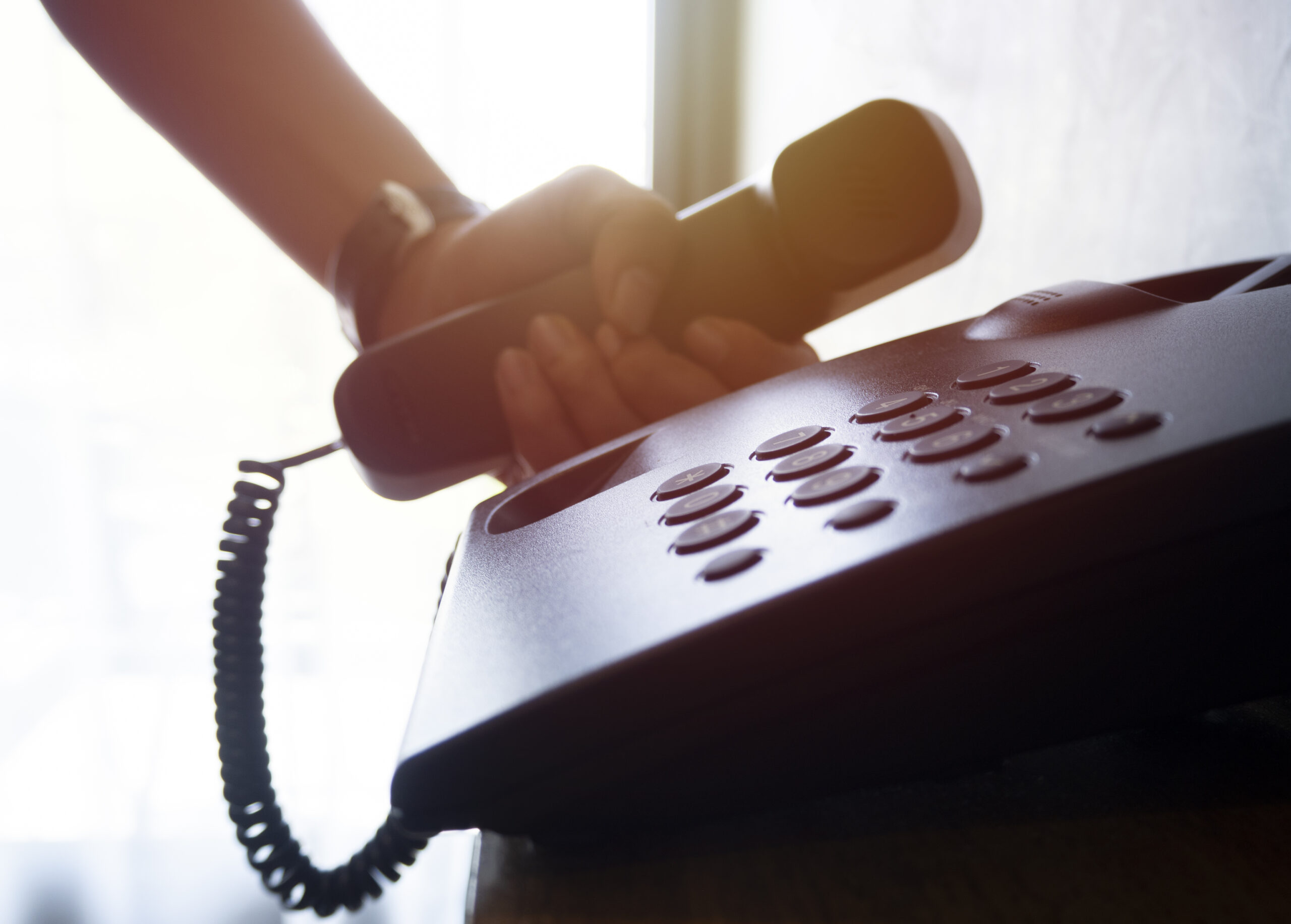 Closeup of landline office telephone with male hand holding its receiver. The businessman calling by phone.
